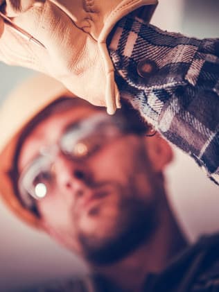 Electrician in a hard hat and safety glasses reaching overhead