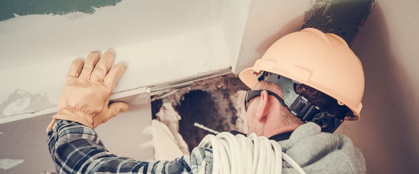 Electrician in a hard hat with a coil of wire working on a ceiling opening